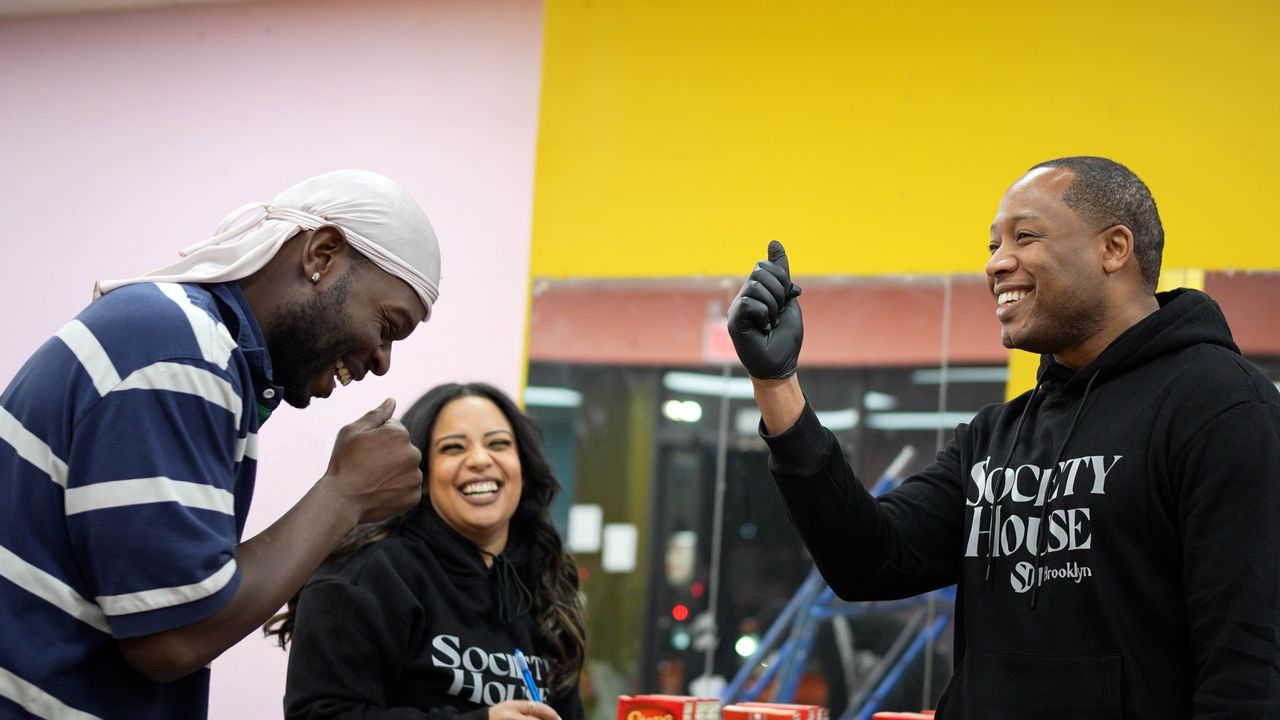 Two staff members of Society House Brooklyn laughing joyfully with a person receiving Thanksgiving meal supplies.