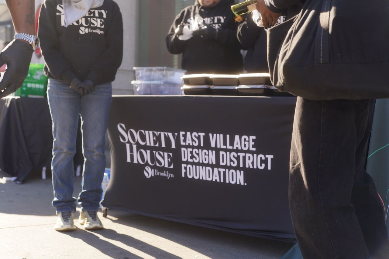Table of prepared to-go meals wrapped in a cover with the Society House Booklyn, and East Village Design District logos.